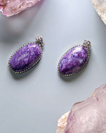 Load image into Gallery viewer, Two Charoite Pendant (Oval Sterling Silver) on a light gray surface with crystals around.