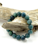 Load image into Gallery viewer, A beaded bracelet made of polished round teal-blue and dark green stones, draped over a piece of natural driftwood on a white background.