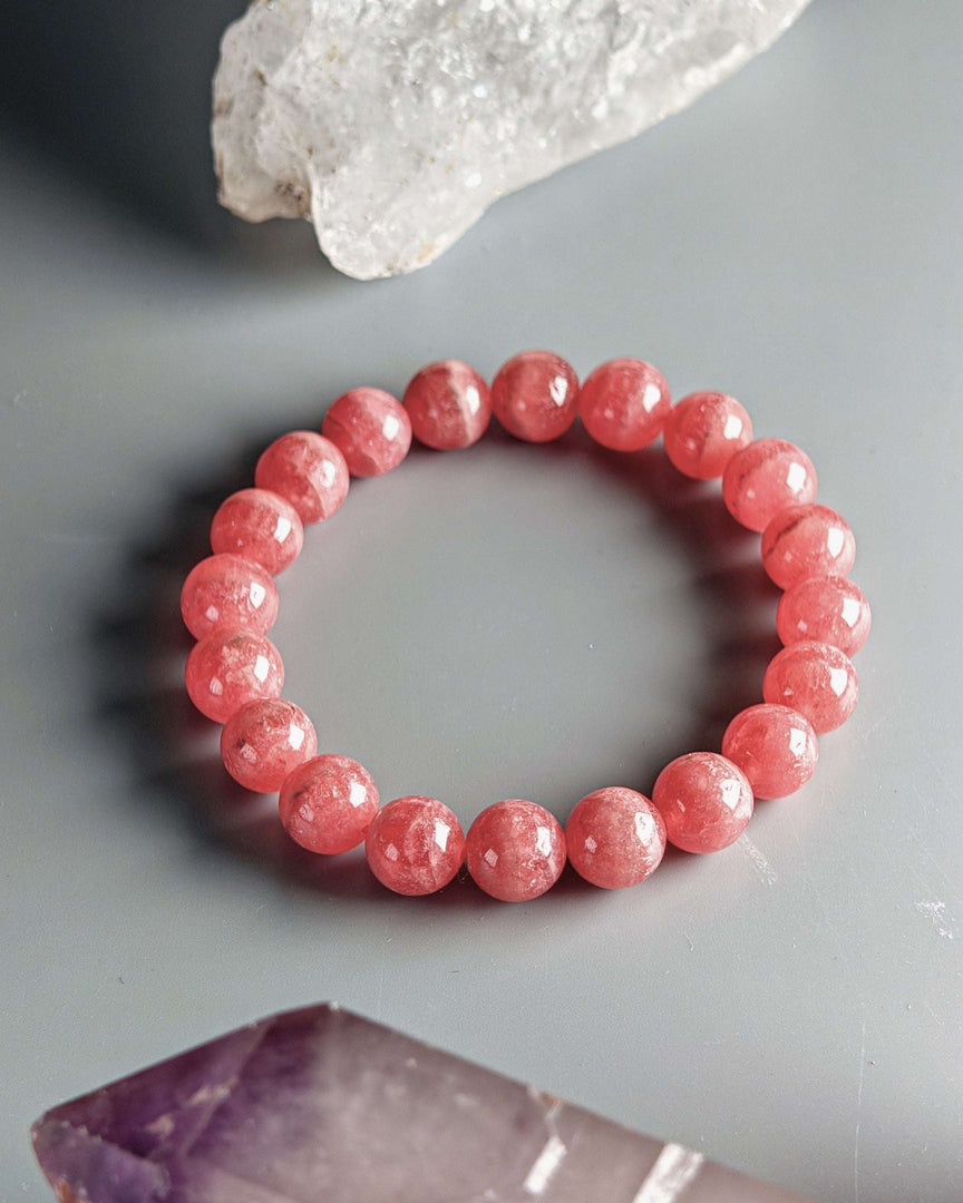 Pink beaded bracelet on a gray surface with crystal rock formations.