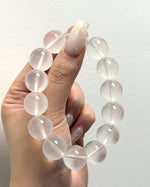 Load image into Gallery viewer, A hand holding a beaded bracelet made of translucent pale pink round gemstone beads against a plain off-white wall.