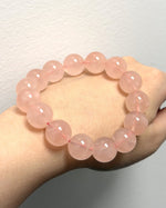 Load image into Gallery viewer, A pink beaded bracelet made of smooth, polished round beads, shown worn on a person's wrist against a plain light gray wall.