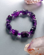 Load image into Gallery viewer, Purple beaded bracelet on a light gray surface with crystals around
