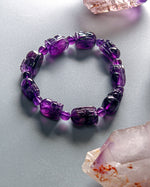Load image into Gallery viewer, Purple beaded bracelet on a light gray surface with crystals around
