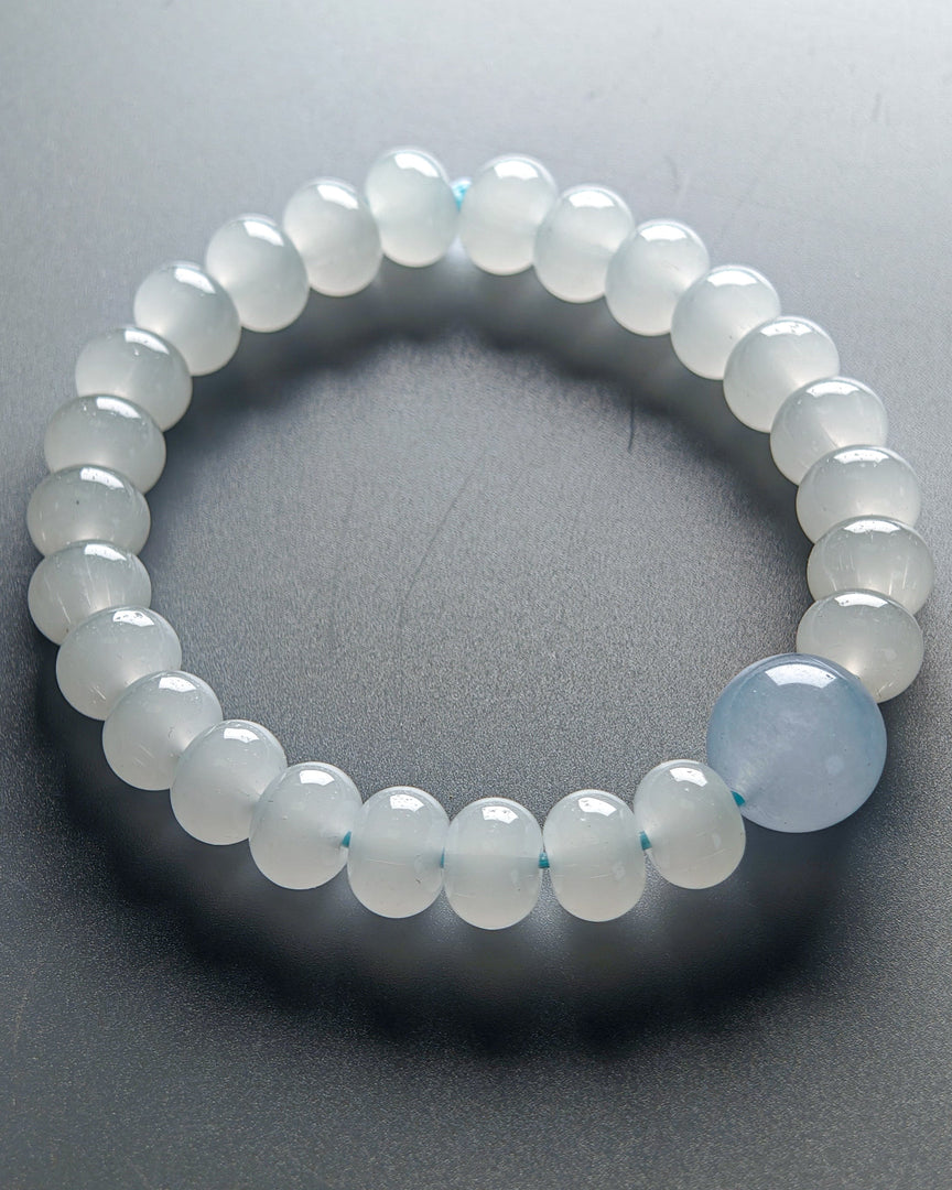 Beaded bracelet with a single blue gemstone on a gray background