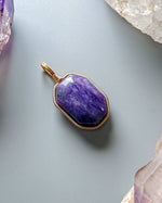 Load image into Gallery viewer, Purple pendant with gold frame on a light gray background with crystals
