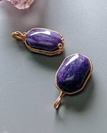 Load image into Gallery viewer, Two purple stone pendants with gold wire wrapping on a gray surface
