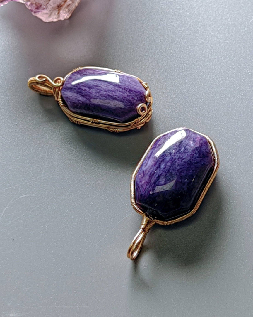 Two purple stone pendants with gold wire wrapping on a gray surface