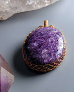 Load image into Gallery viewer, Purple stone pendant with gold wire wrapping on a gray surface with crystals.
