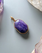 Load image into Gallery viewer, Purple pendant with gold frame on a light gray background with crystals
