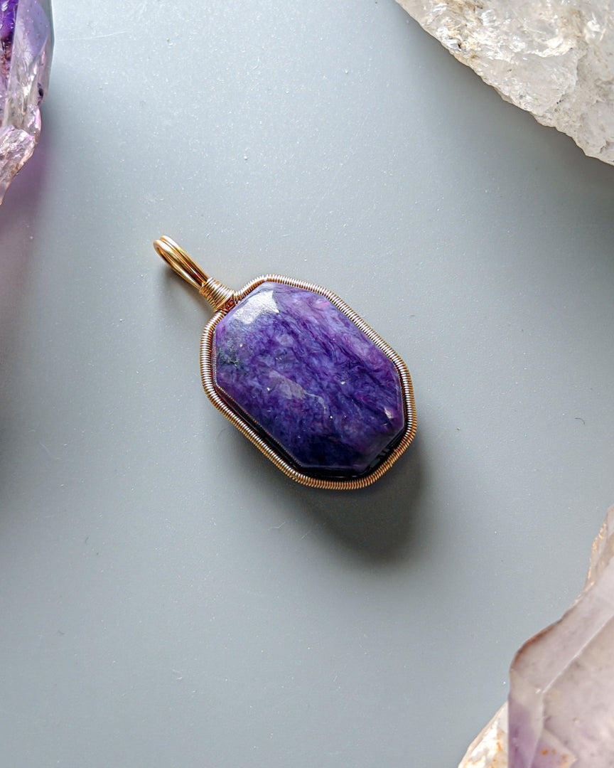Purple pendant with gold frame on a light gray background with crystals