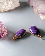 Load image into Gallery viewer, Two purple stone pendants with gold wire wrapping on a light gray surface with crystal rocks.
