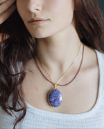 Load image into Gallery viewer, Woman wearing a necklace with a purple pendant against a dark background
