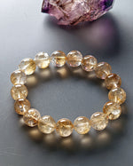 Load image into Gallery viewer, Beaded bracelet with yellow gemstones on a gray surface with crystals in the background
