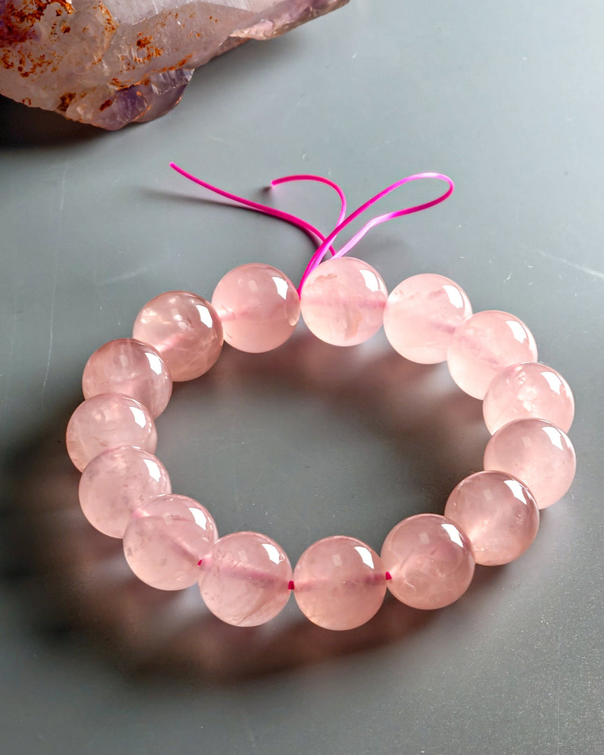 Madagascar Rose Quartz Bracelet on a gray surface with a crystal in the background