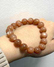 A beaded stretch bracelet made of smooth, polished round beads in a warm peachy-brown color, worn on a person's wrist against a plain light gray wall.