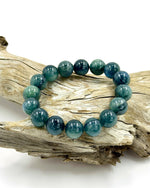 Load image into Gallery viewer, A beaded stretch bracelet made of polished round teal and blue-green stones, displayed on a piece of weathered driftwood against a clean white background.