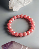 Load image into Gallery viewer, Pink beaded bracelet on a gray surface with crystal rock formations.
