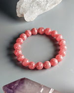 Load image into Gallery viewer, Pink beaded bracelet on a gray surface with crystal rock formations.
