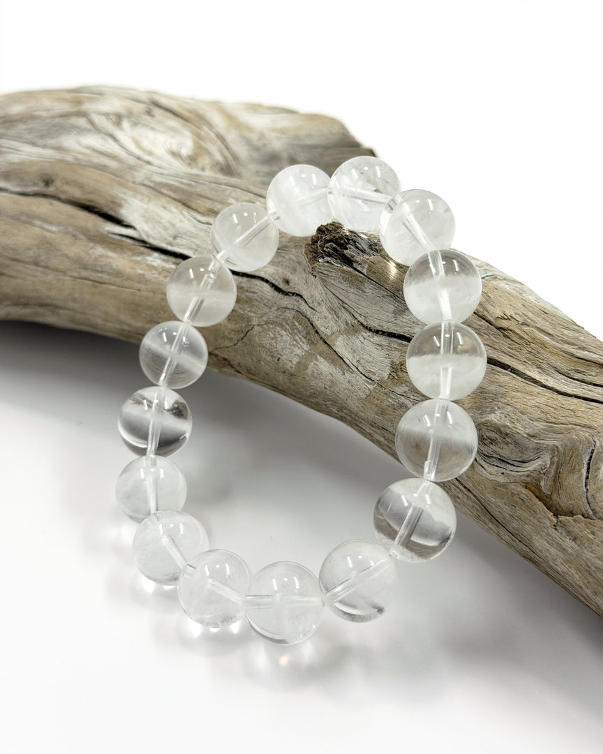 Clear beaded bracelet on a piece of driftwood with a white background