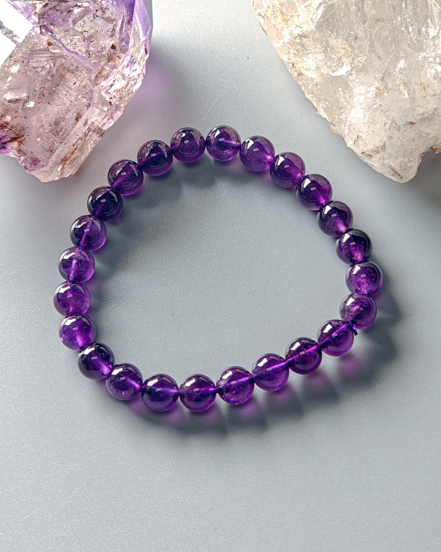 Purple beaded bracelet on a light gray surface with crystal rocks.