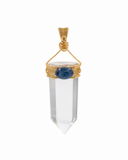 A clear crystal point pendant with a gold wire-wrapped setting and a central oval blue gemstone, shown on a plain white background.
