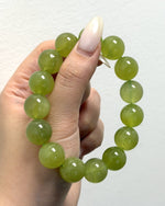 Load image into Gallery viewer, A beaded stretch bracelet made of smooth, translucent light green jade-like beads, held in a hand with long, manicured nails against a plain white wall.