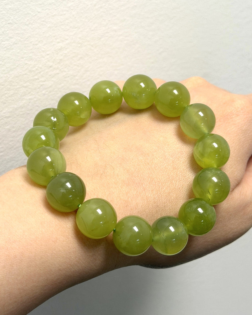 A beaded stretch bracelet made of glossy, translucent light green round beads, shown worn on a person's wrist against a plain light gray wall.