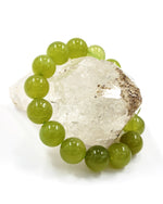 Load image into Gallery viewer, A beaded bracelet made of glossy light green gemstone-like beads, arranged around a clear quartz crystal on a white background.