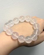 Load image into Gallery viewer, A translucent pale pink beaded bracelet worn on a person's wrist against a plain light gray wall.