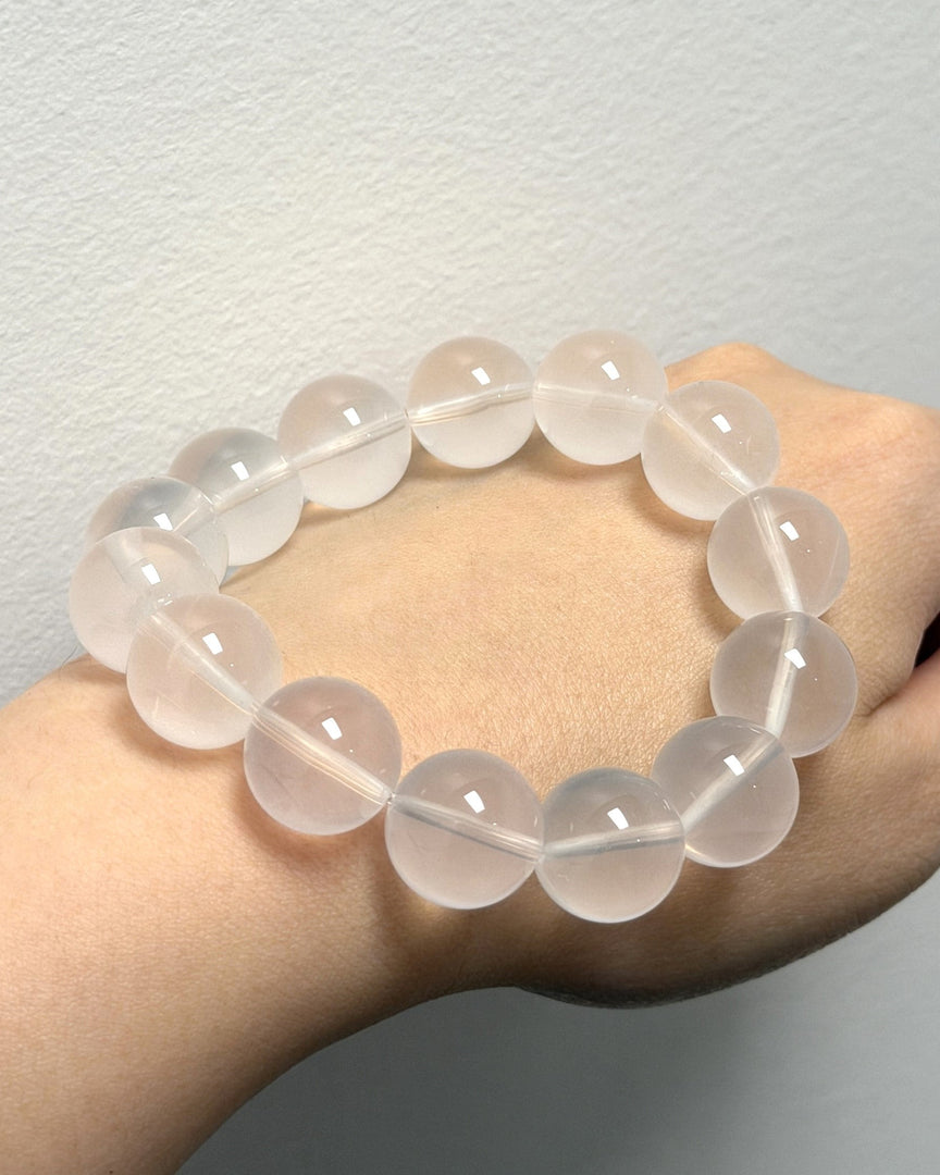 A translucent pale pink beaded bracelet worn on a person's wrist against a plain light gray wall.