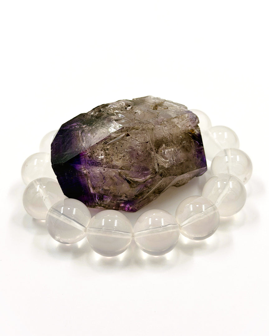 A beaded bracelet made of translucent white oval beads arranged in a circle around a rough, faceted purple and gray crystal on a clean white background.