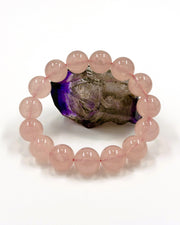 A pink beaded bracelet made of smooth, polished round beads, displayed in a ring shape around a dark, polished crystal specimen on a clean white background.