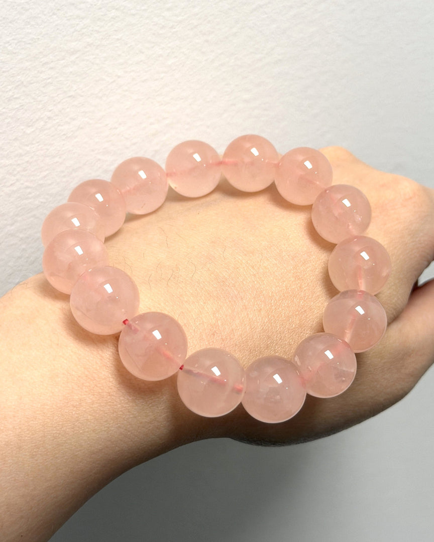 A pink beaded bracelet made of smooth, polished round beads, shown worn on a person's wrist against a plain light gray wall.