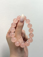 Load image into Gallery viewer, A hand holding a beaded bracelet made of smooth, translucent light pink round beads against a plain off-white background.