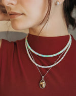 Load image into Gallery viewer, Close-up of a person wearing multiple necklaces with a pendant on a red background
