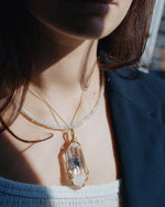 Load image into Gallery viewer, Close-up of a person wearing a gold necklace with a clear pendant.
